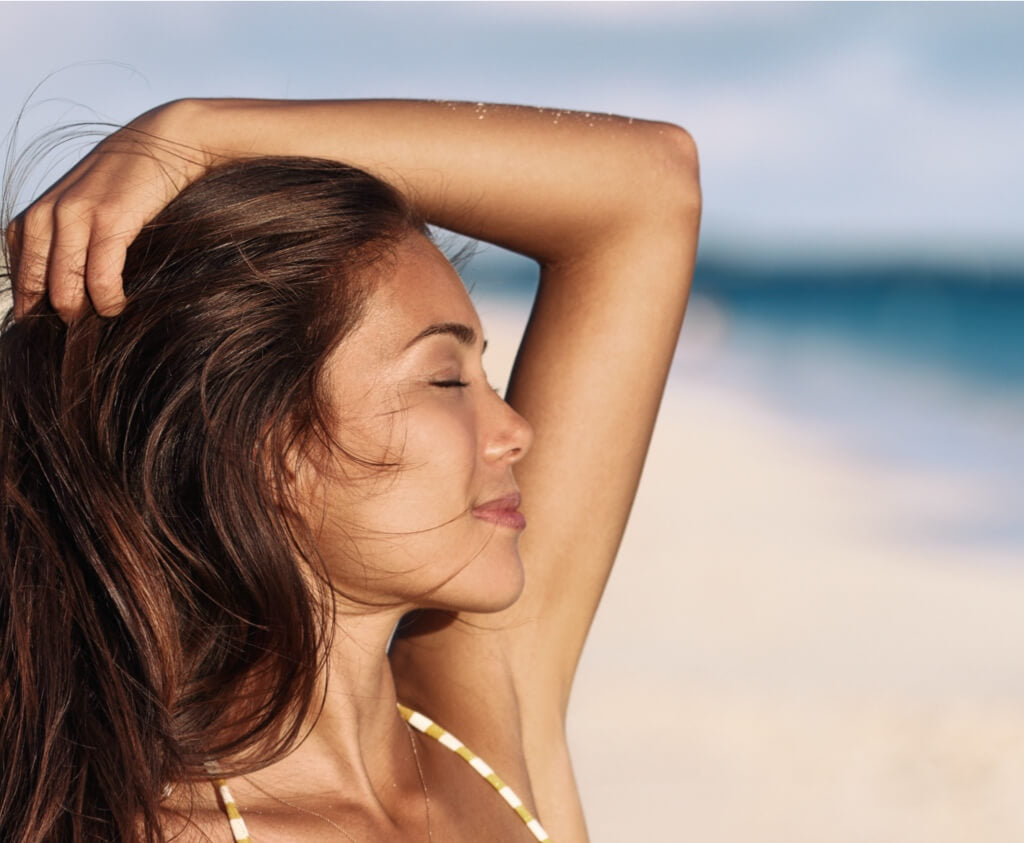 Lady enjoying sunshine on a beach - links to sun screen for your skin type blog